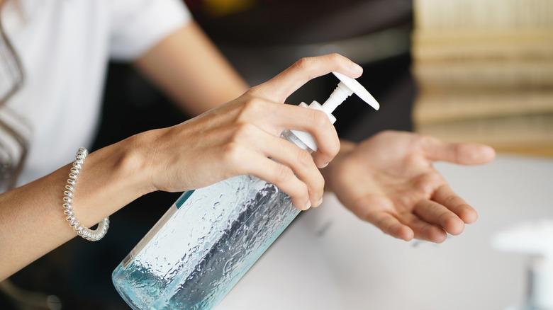 A hand squirting antibacterial soap onto another hand before washing at a sink.