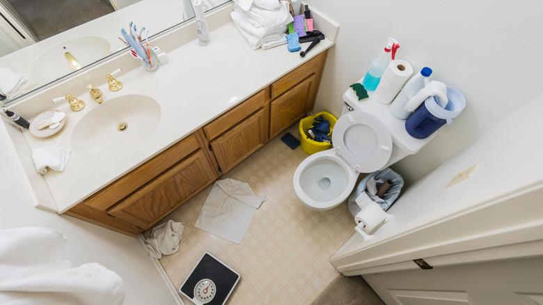 An aerial view of a messy bathroom with skincare, cleaning products, and other objects on surfaces.