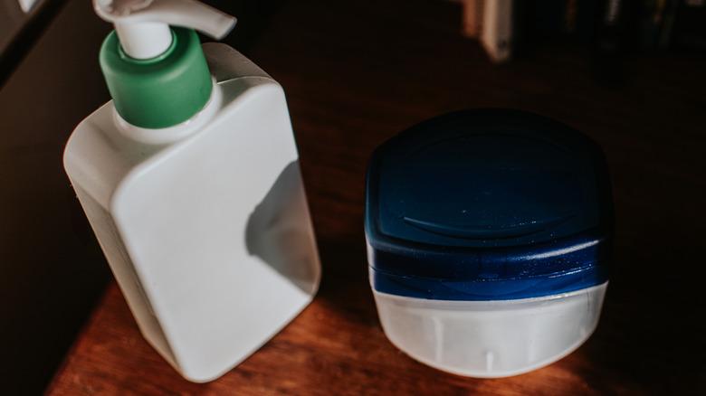A bottle of lotion and a tub of petroleum jelly that resembles Vaseline sitting on a table.