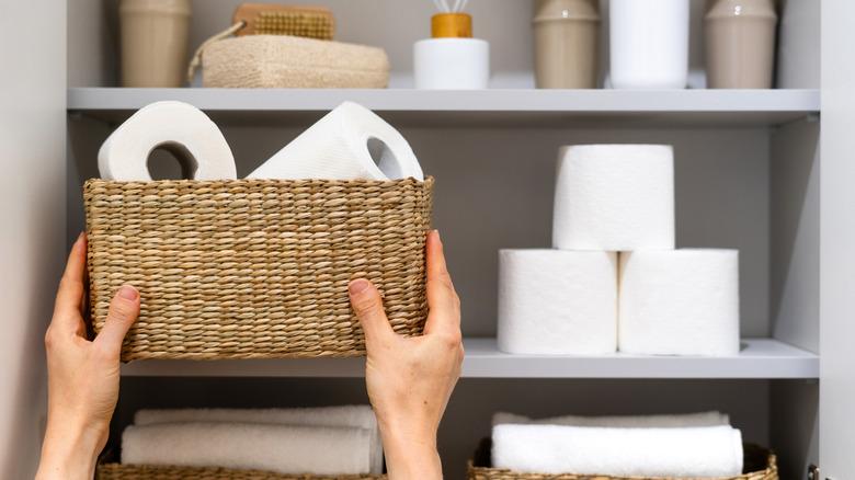 Hands reaching up to store a basket full of toilet paper.