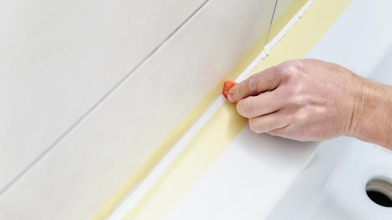 hand smoothing silicone sealant with painters tape to get sharp lines