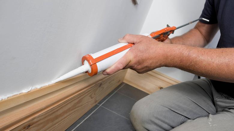 man caulking along wooden baseboard