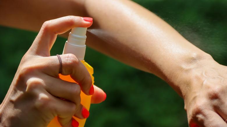 person using a spray bottle to apply mosquito repellent
