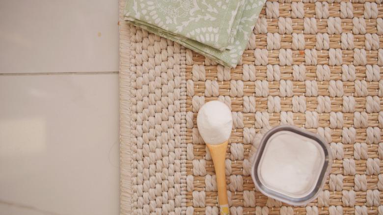 floor rug with baking soda in bowl and spoon sitting on top with a green patterned towel and tile floor