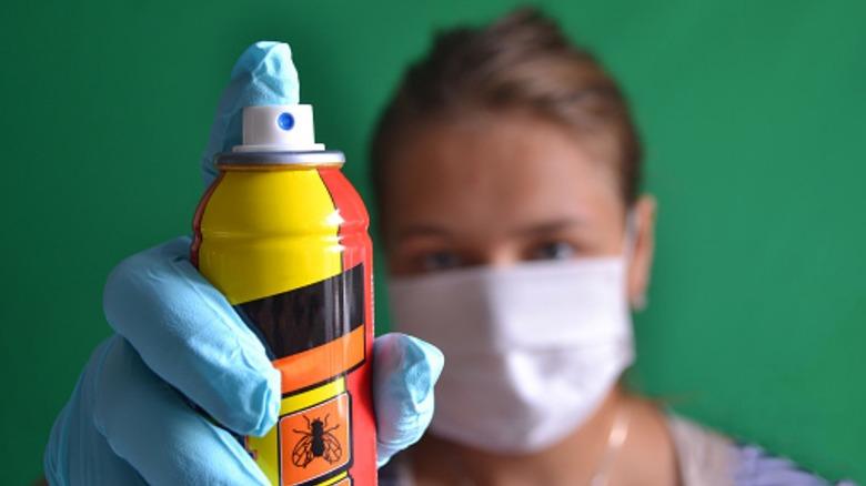 Woman spraying insecticide while wearing PPE