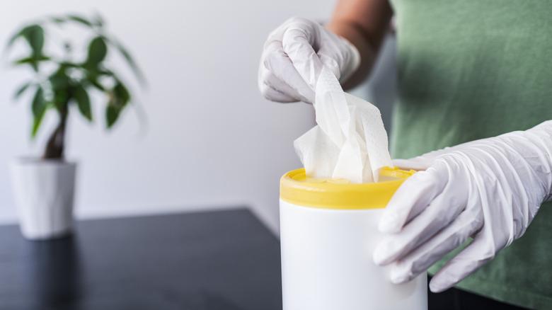 person wearing gloves pulling disinfectant wipes out of container